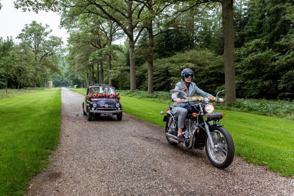 bruidspaar in zwarte fiat 500 met motorrijder ervoorr