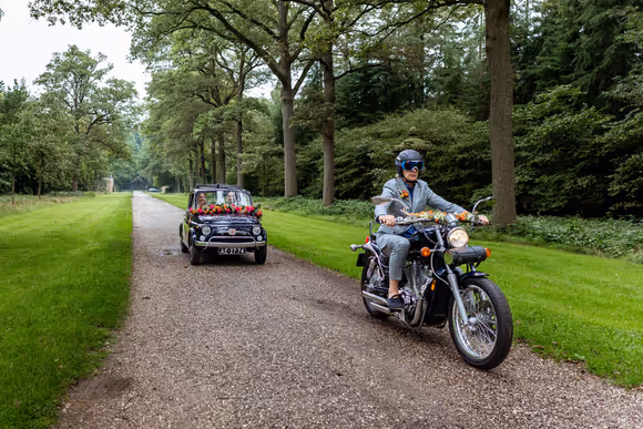 bruidspaar in zwarte fiat 500 met motorrijder ervoorr